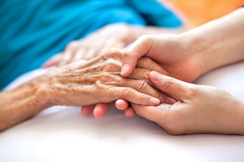 Woman holding senior woman's hand on bed - Willow Park Convalescent Home concept