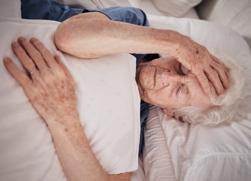 senior woman in bed at retirement home holding her head in pain