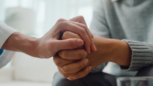 Closeup of young females hands clasped with someone placing a hand on top in show of support